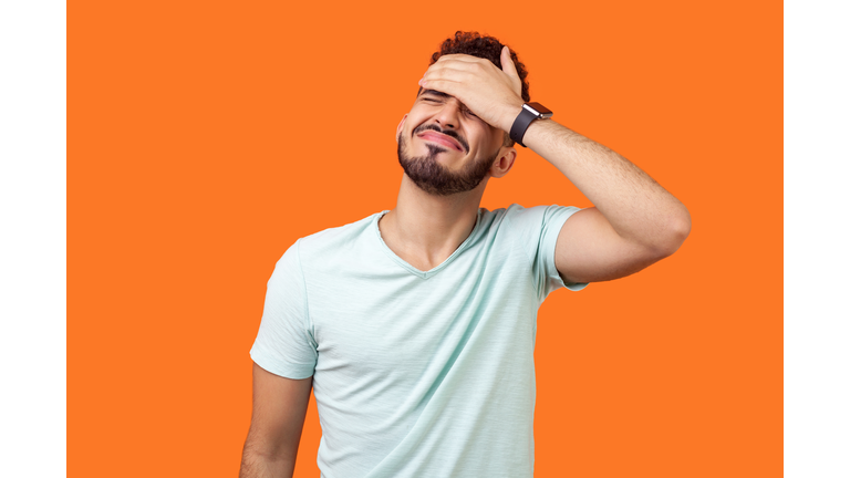 Facepalm. Portrait of desperate brunette man covering face with hand. indoor studio shot isolated on orange background