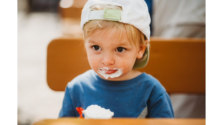 Young white child eating ice cream with dirty mouth and cap