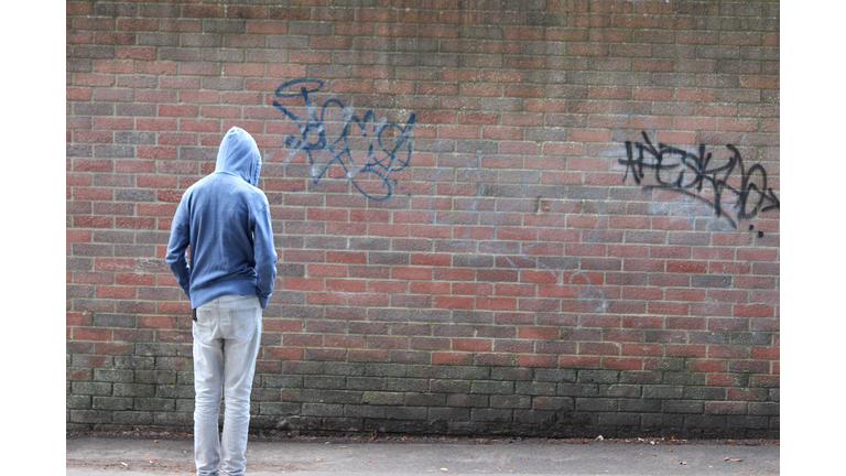 Image of teenage boy / youth wearing hoodie, beside graffiti wall