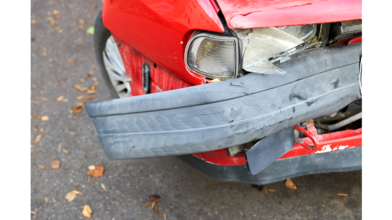 Closeup detail of crashed red car front headlight fender wheel and deformed bumper. Concept of road safety while driving while intoxicated.