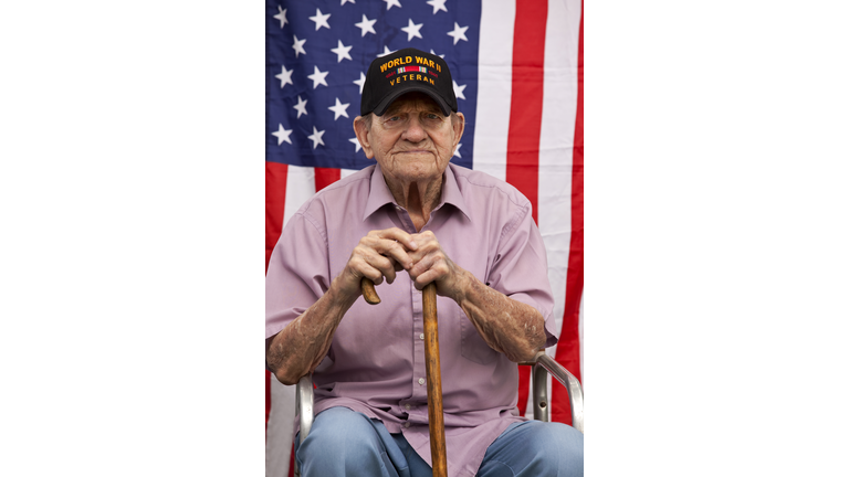 World War Two, Veteran wearing  baseball cap with text, "World War Two Veteran". Sitting in front of American Flag