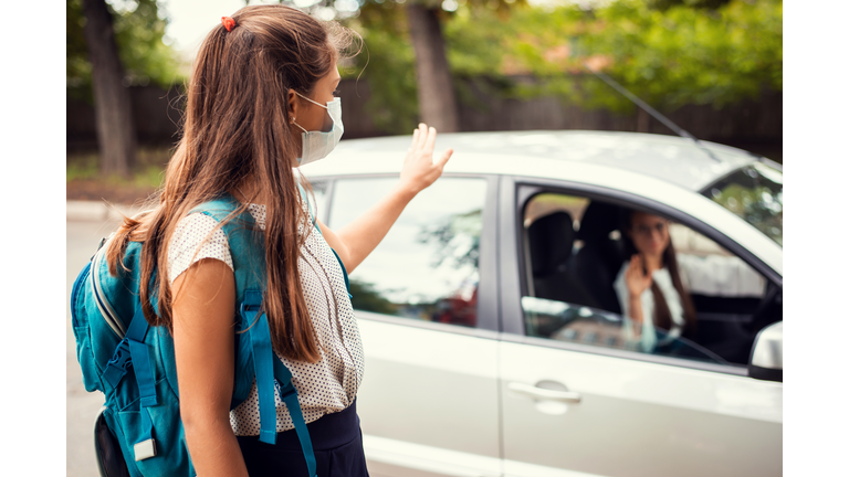 Mother in car, dropping off her daughter to the school and wishing her a good day. Back to school, motherhood concept.