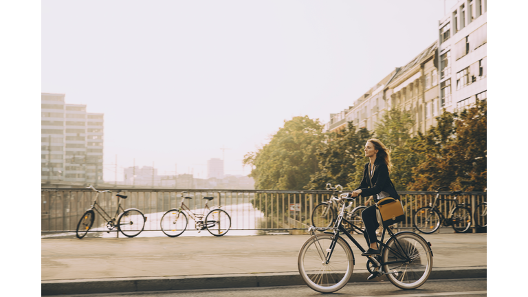 Full length of female professional riding bicycle on road in city against sky