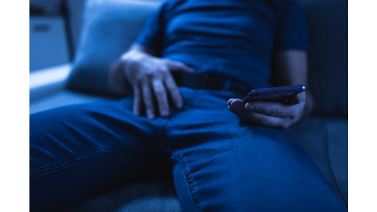 Man holding modern smartphone / cellphone and watching XX videos on a home couch. Taboo still in modern times.