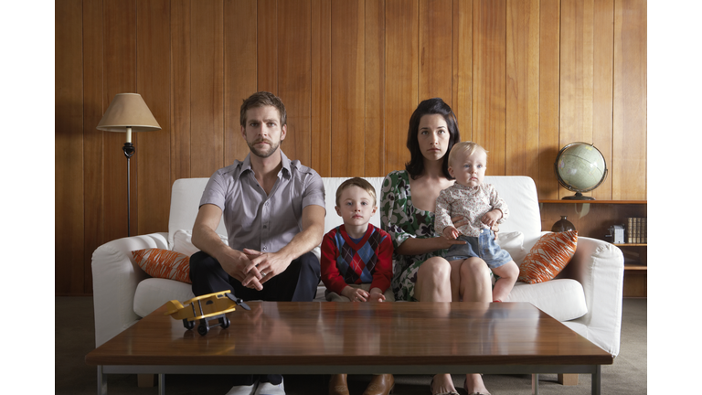Parents with son (3-5), and baby girl (6-9 months) sitting on couch in living room
