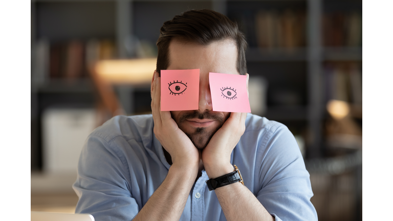 Employee hides eyes with sticky notes wants sleep at workplace