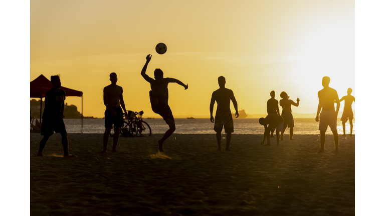 Silhouette of young people playing beach soccer
