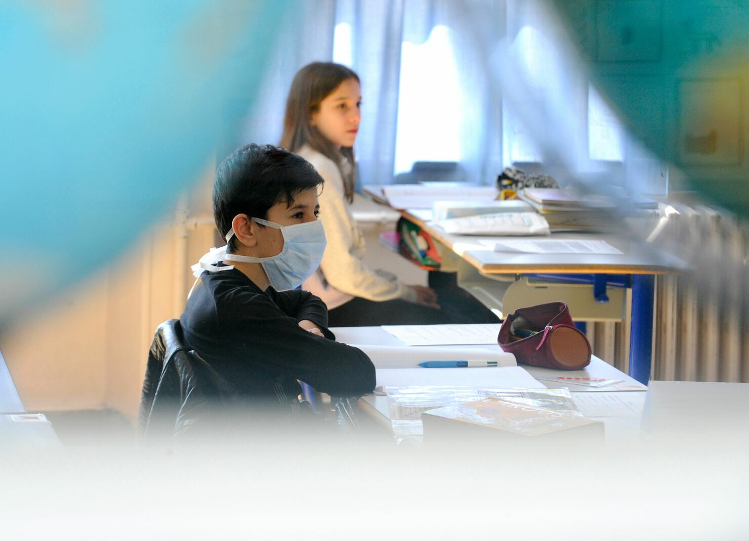Boy sits at desk with mask on