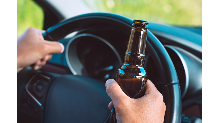 Closeup of drunk driver hands on the steering wheel with a bottle of beer. Driving under alcohol influence