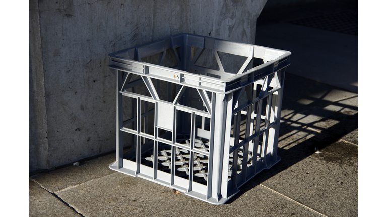 Empty grey plastic milk crate on a tiled sidewalk in a city street