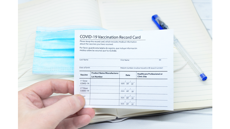 Womans hand holds coronavirus vaccination record card on background blue medical mask