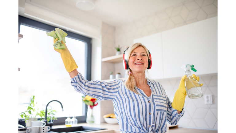 Portrait of senior woman with headphones and gloves cleaning indoors at home.