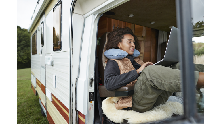 Woman with neck pillow using laptop in motor van