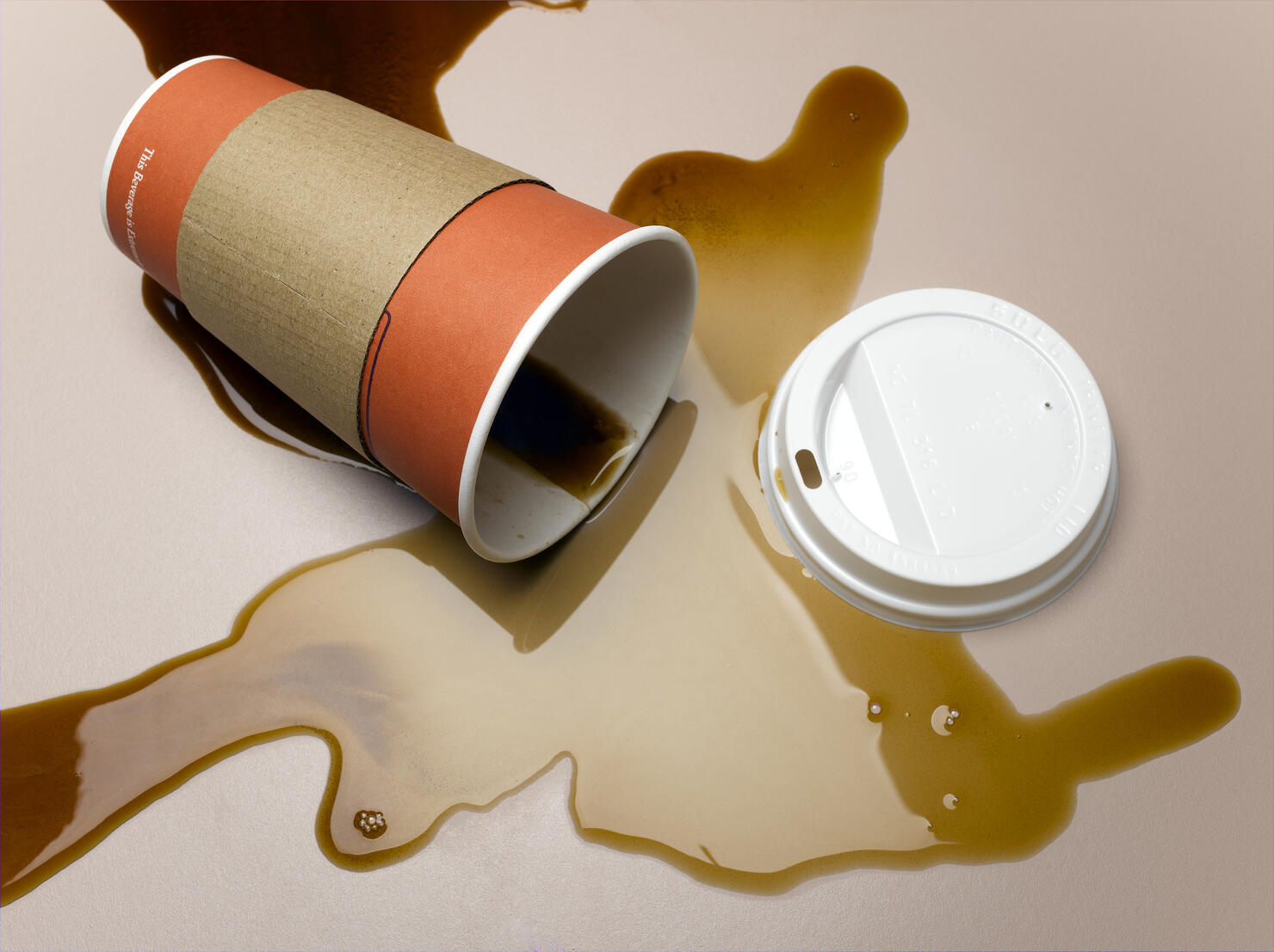 Vending cup on side spilling coffee onto surface, elevated view, close-up