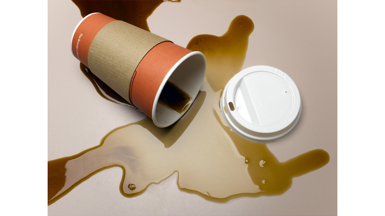 Vending cup on side spilling coffee onto surface, elevated view, close-up