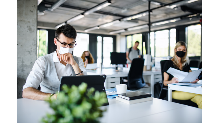 Young people with face masks back at work or school in office after lockdown.