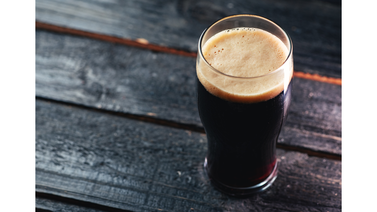 A glass of dark craft beer porter on a wooden table in a pub with copyspace