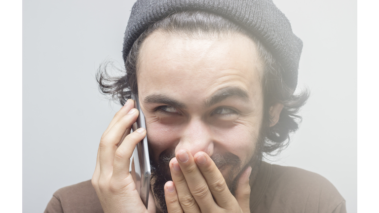 Smirking young man talking on phone over gray background