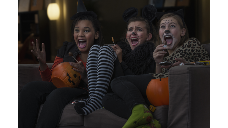Girls in costumes watching scary movie together on Halloween