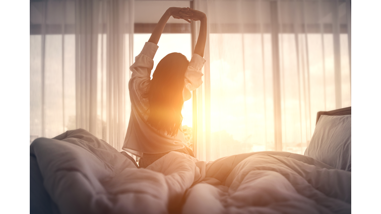 Happy woman stretching in bed after waking up. Happy young girl greets good day.