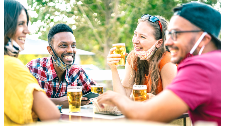 Friends drinking beer with opened face masks - New normal lifestyle concept with people having fun together talking on happy hour at brewery bar - Bright vivid filter with focus on afroamerican guy