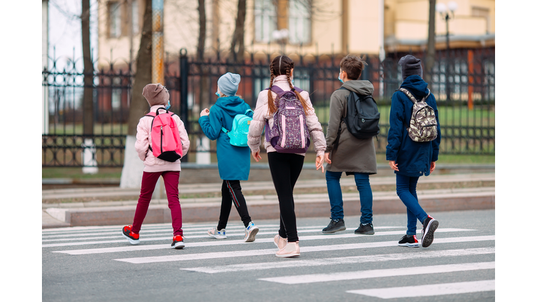 School children cross the road in medical masks. Children go to school.