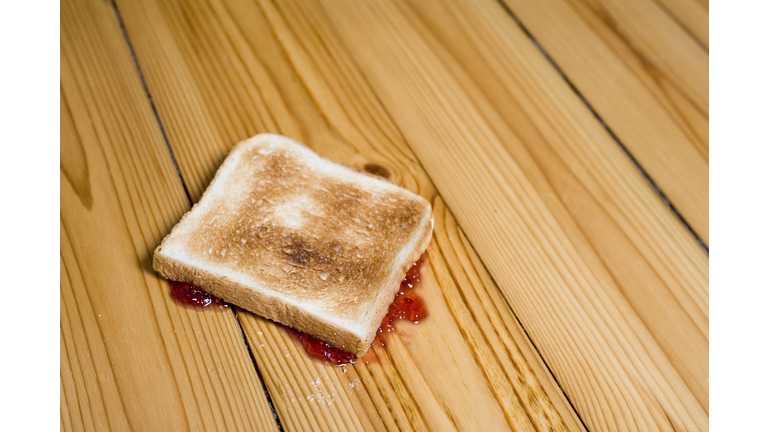 Slice of toast with strawberry jam turned upside down on floor