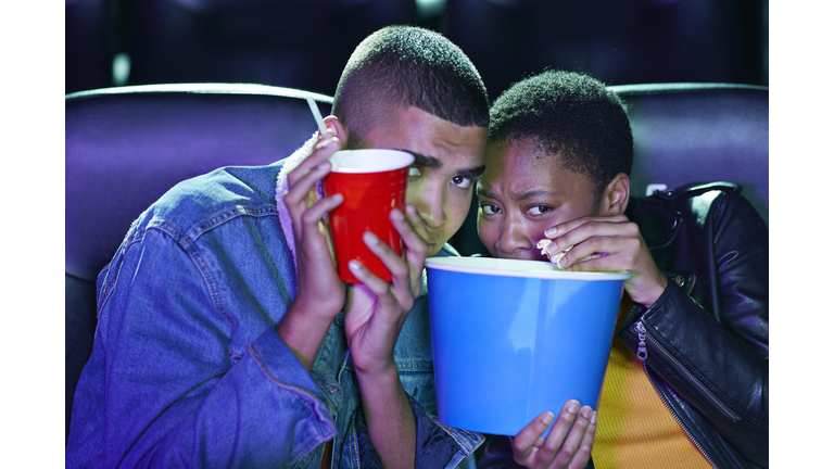 Frightened young couple hiding while watching horror movie together at cinema theater