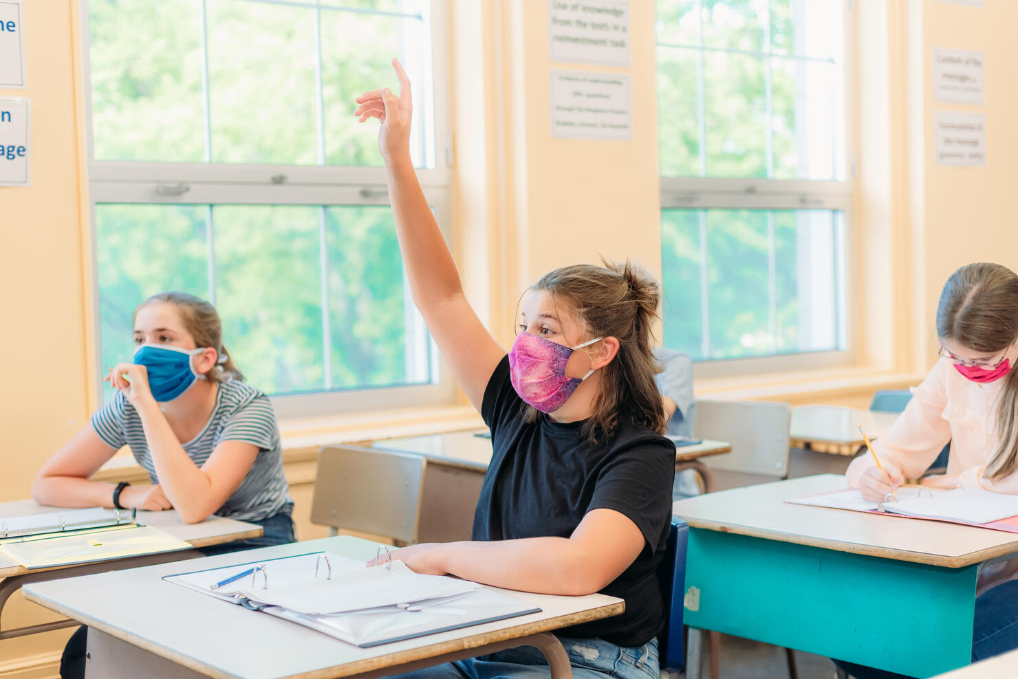 A thirteen year old girl is sitting at her desk in class with a mask to protect herself from Covid-19.