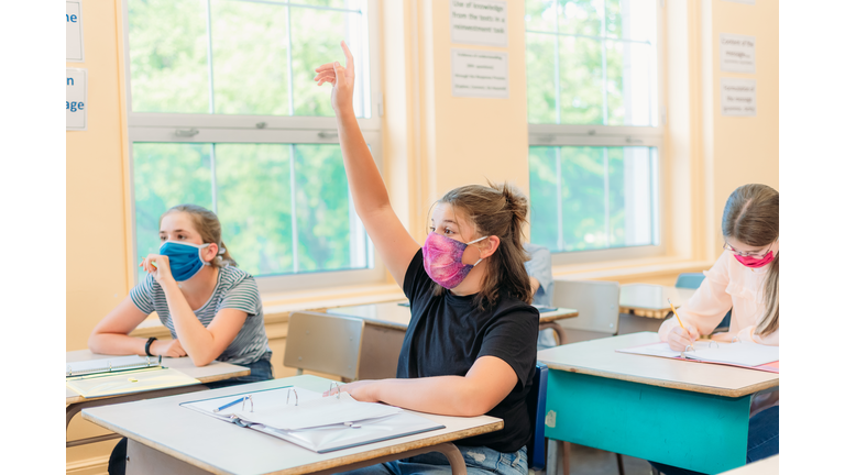 A thirteen year old girl is sitting at her desk in class with a mask to protect herself from Covid-19.