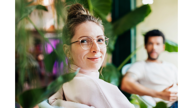 Portrait Of Woman Sitting Between Plants In Café