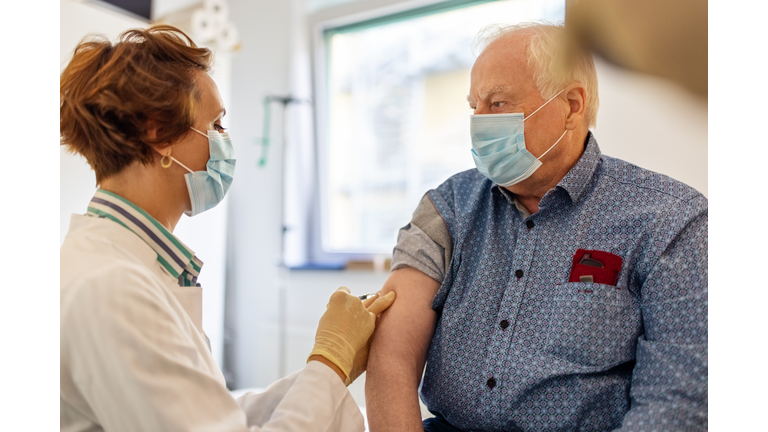 General practitioner giving flu shot to a senior man in clinic