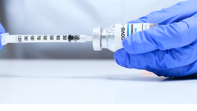 Female doctor hands in blue medical gloves with transparent liquid coronavirus vaccine bottle and syringe for injection in the laboratory. Research and development of new cure for diseases