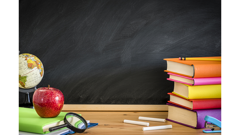 Teacher desk full of books against a blackboard background whit copy space