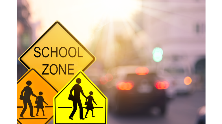 School zone warning sign on blur traffic road with colorful bokeh light abstract background. Copy space of transportation and travel concept. Vintage tone color style.