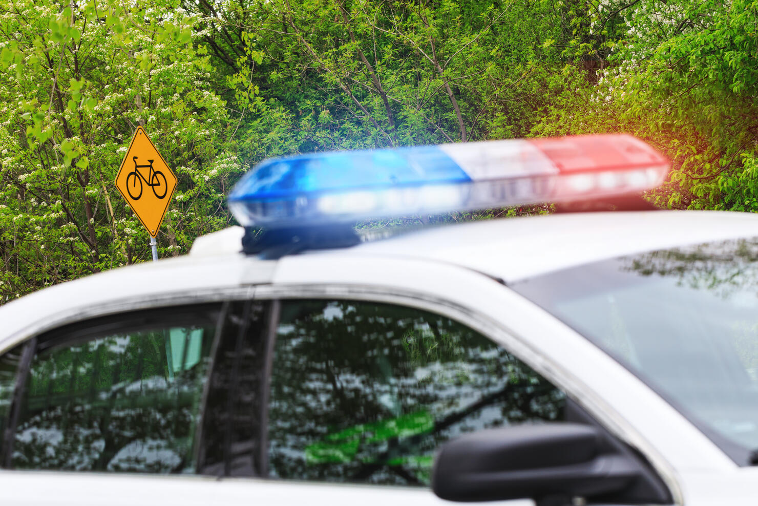 Bicycle or bike road sign with selective focus & police car with activated siren lights in blurred plan. A police patrol supervises the road reserved for cyclists or bicyclers.