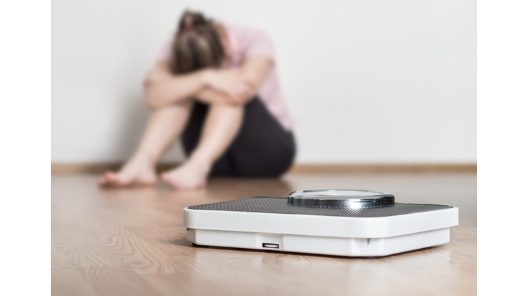 Weight loss fail concept. Scale and depressed, frustrated and sad woman sitting on floor holding head and arms on knees.