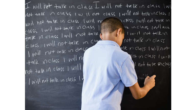 Hispanic boy writing punishment on blackboard