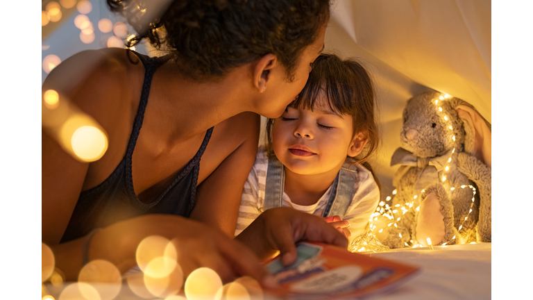 Loving ethnic mother kissing daughter in cozy hut