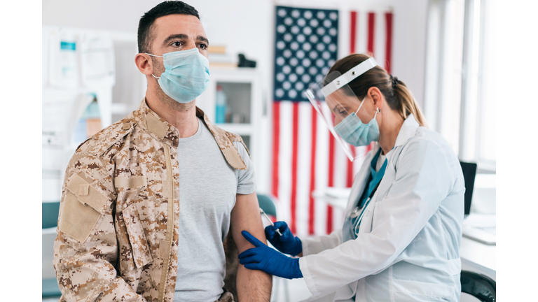 Doctor wearing protective work wear injecting COVID-19  vaccine to soldier