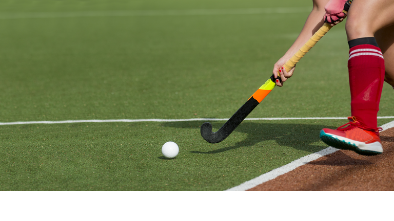 Female field hockey player passing to a team mate on a modern, water artificial astroturf field.