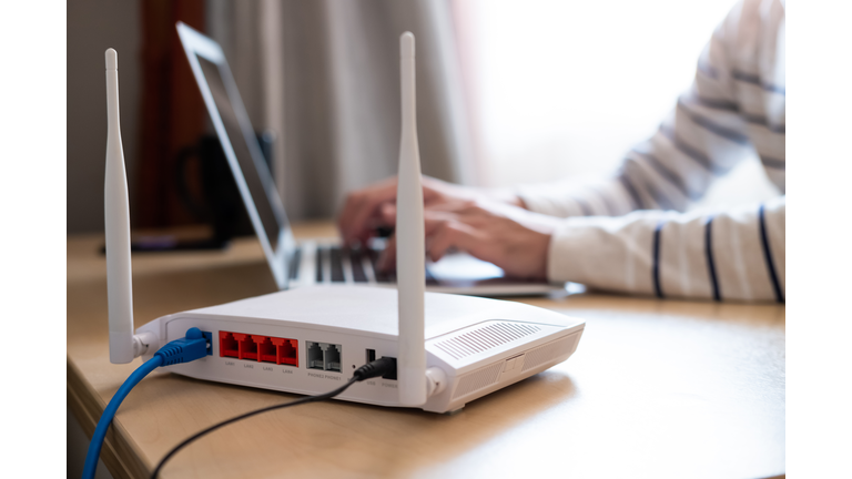 Selective focus at router. Internet router on working table with blurred man connect the cable at the background. Fast and high speed internet connection from fiber line with LAN cable connection.