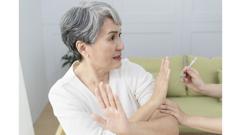 refusing vaccine injection into senior woman shoulder,She showed a  scared expression.