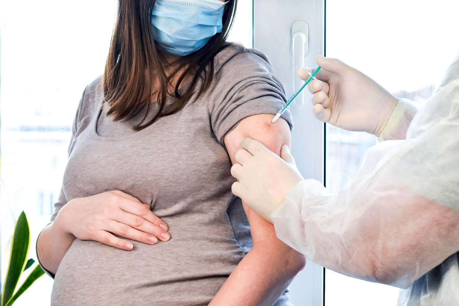 Doctor giving COVID -19 coronavirus vaccine injection to pregnant woman. Doctor Wearing Blue Gloves Vaccinating Young Pregnant Woman In Clinic. People vaccination concept.