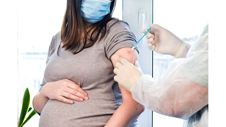 Doctor giving COVID -19 coronavirus vaccine injection to pregnant woman. Doctor Wearing Blue Gloves Vaccinating Young Pregnant Woman In Clinic. People vaccination concept.