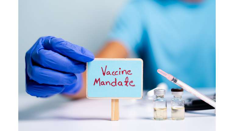 Concept of coronavirus or covid-19 vaccine mandate, showing with doctor hands with gloves by placing sign board next to vaccine shots and syringe