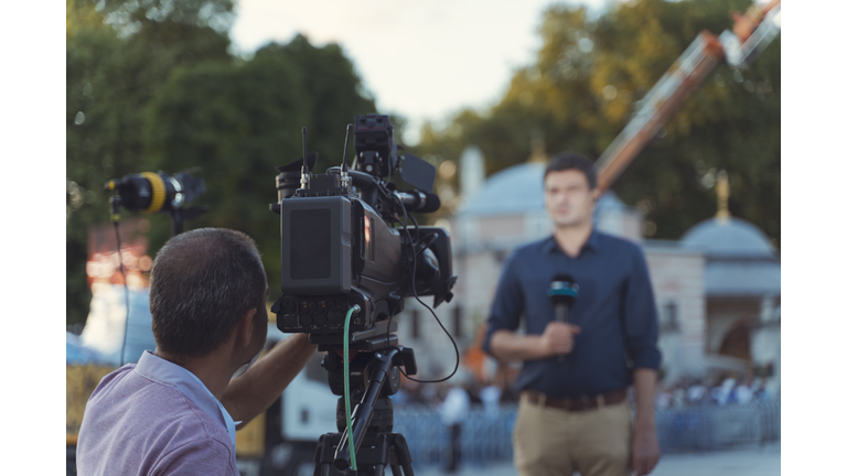 Behind the scene concept. Cameraman working on professional camera taking TV interviewer, professional news reporter making news outdoors.