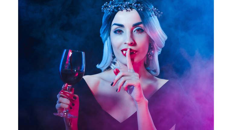 vampire holding wineglass with blood and showing silence symbol on darkness with smoke