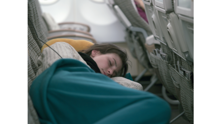 Young Woman Sleeping In Airplane Cabin On Long Distance Flight