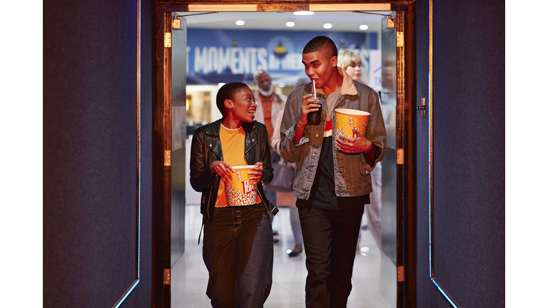 Happy young friends talking while walking in corridor at movie theater